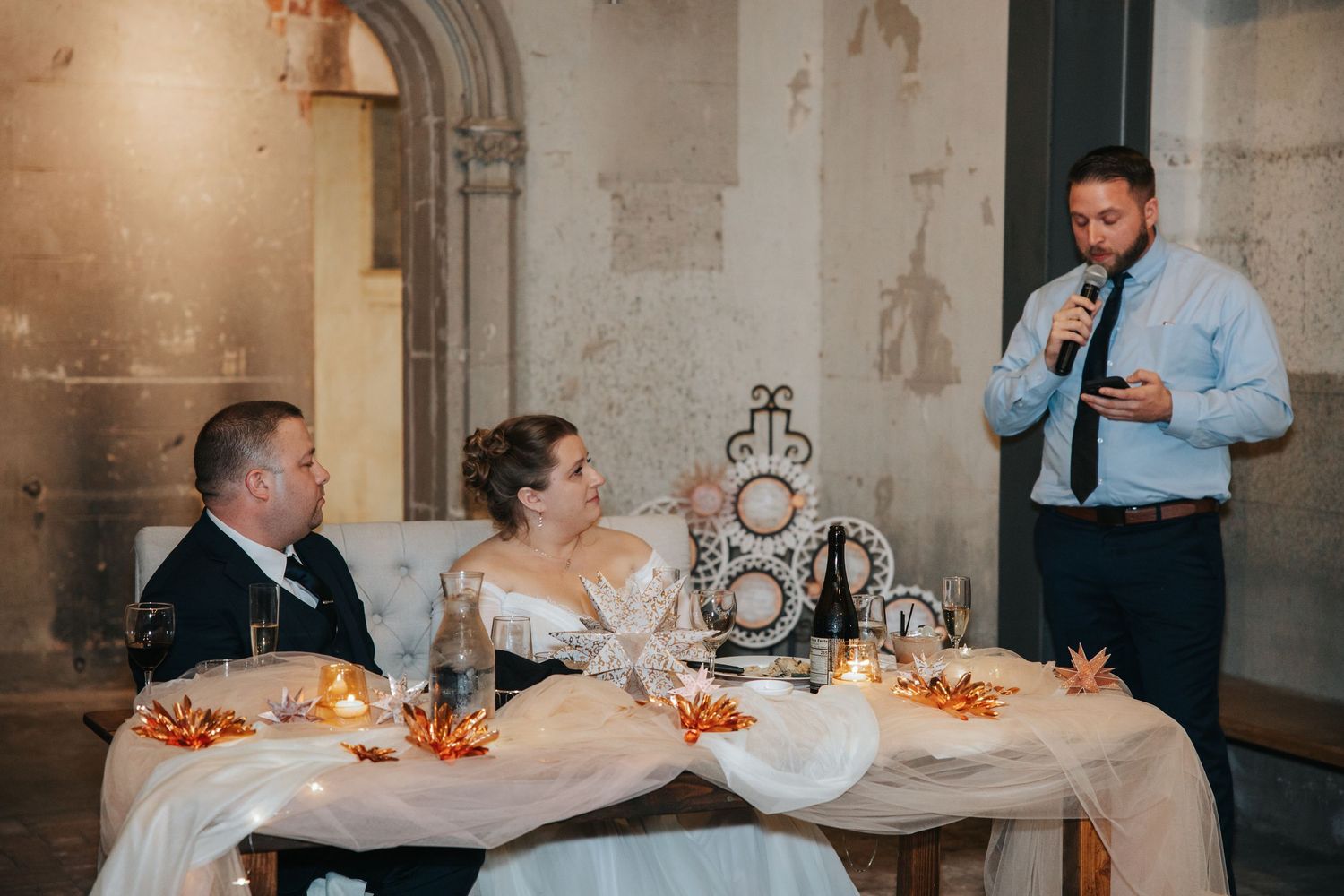 Wedding guests enjoy a formal dinner reception at an elegant venue with stone walls and warm lighting.