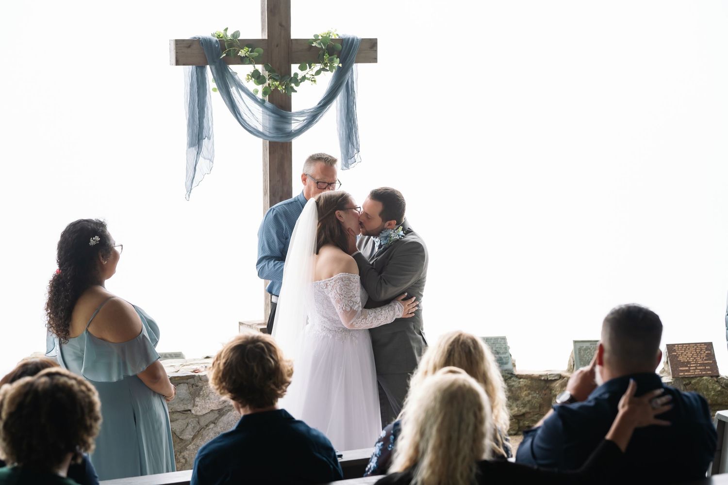 A couple exchanges vows during a wedding ceremony in front of large windows overlooking a scenic outdoor view.