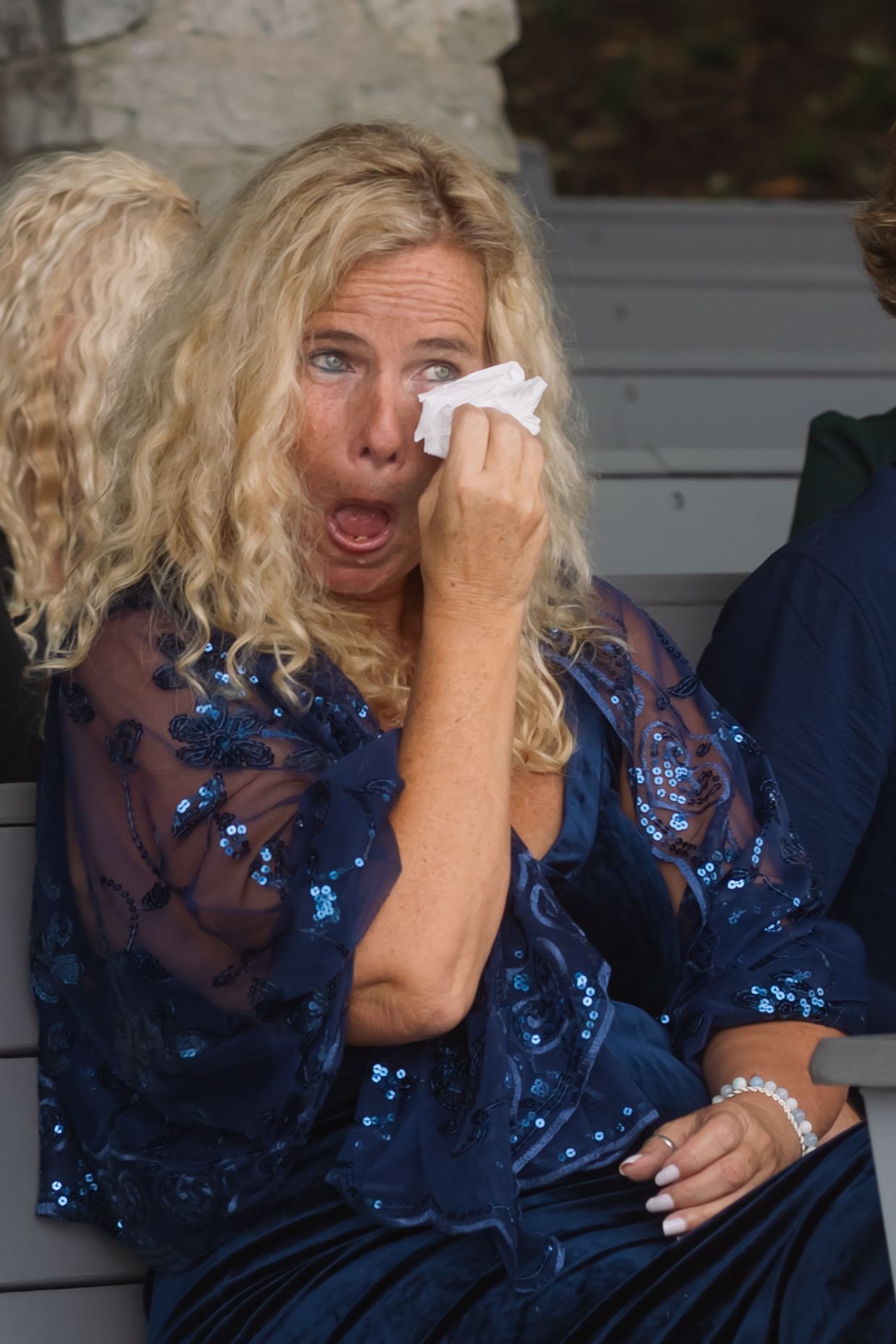 Person in a sparkly blue evening dress wipes tears with tissue while displaying strong emotion.