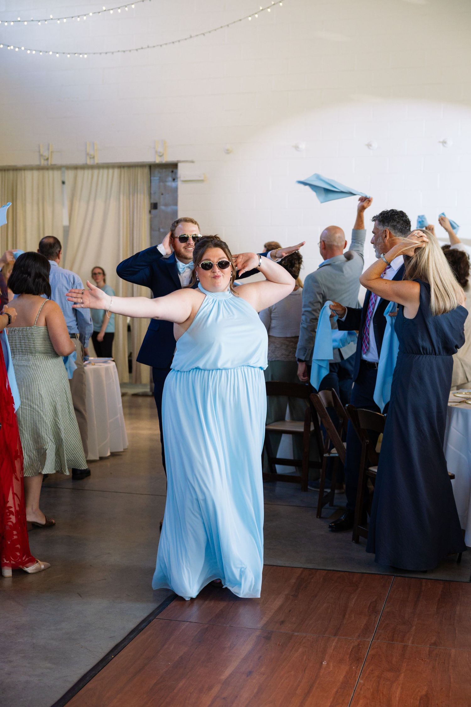 Wedding guests perform synchronized dance moves in a reception hall during a group dance activity.