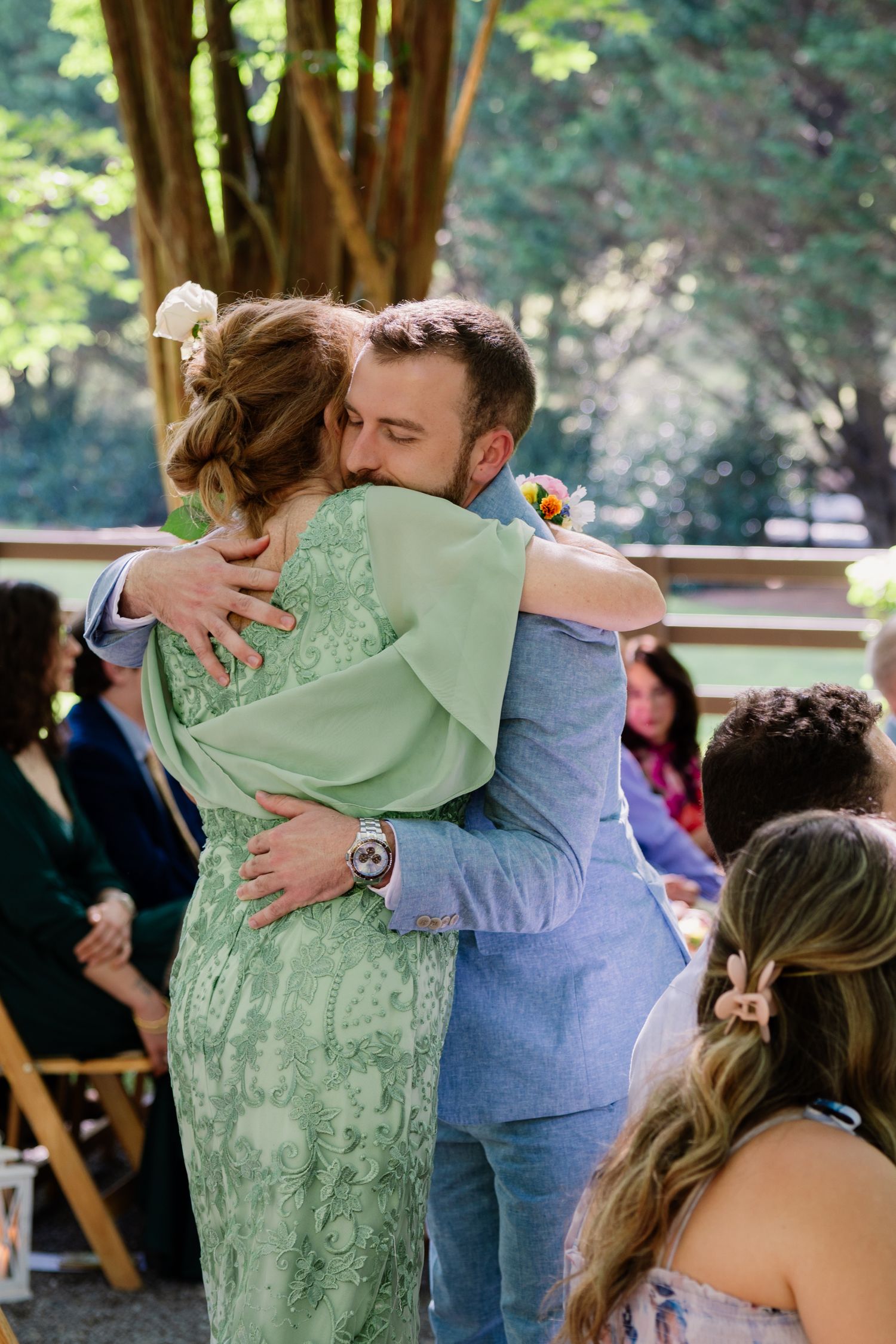 Wedding attendees share emotional embraces during a celebration in an outdoor garden setting.