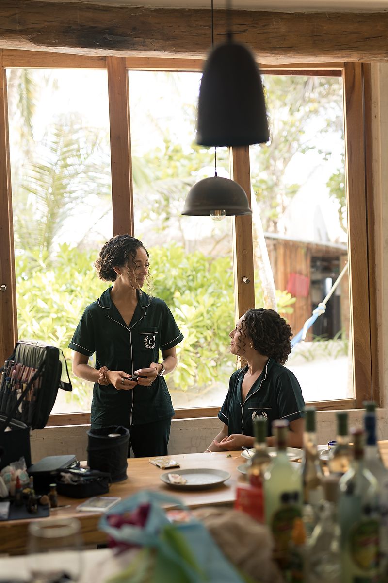 People working at a long wooden table in a sunlit room with large windows.