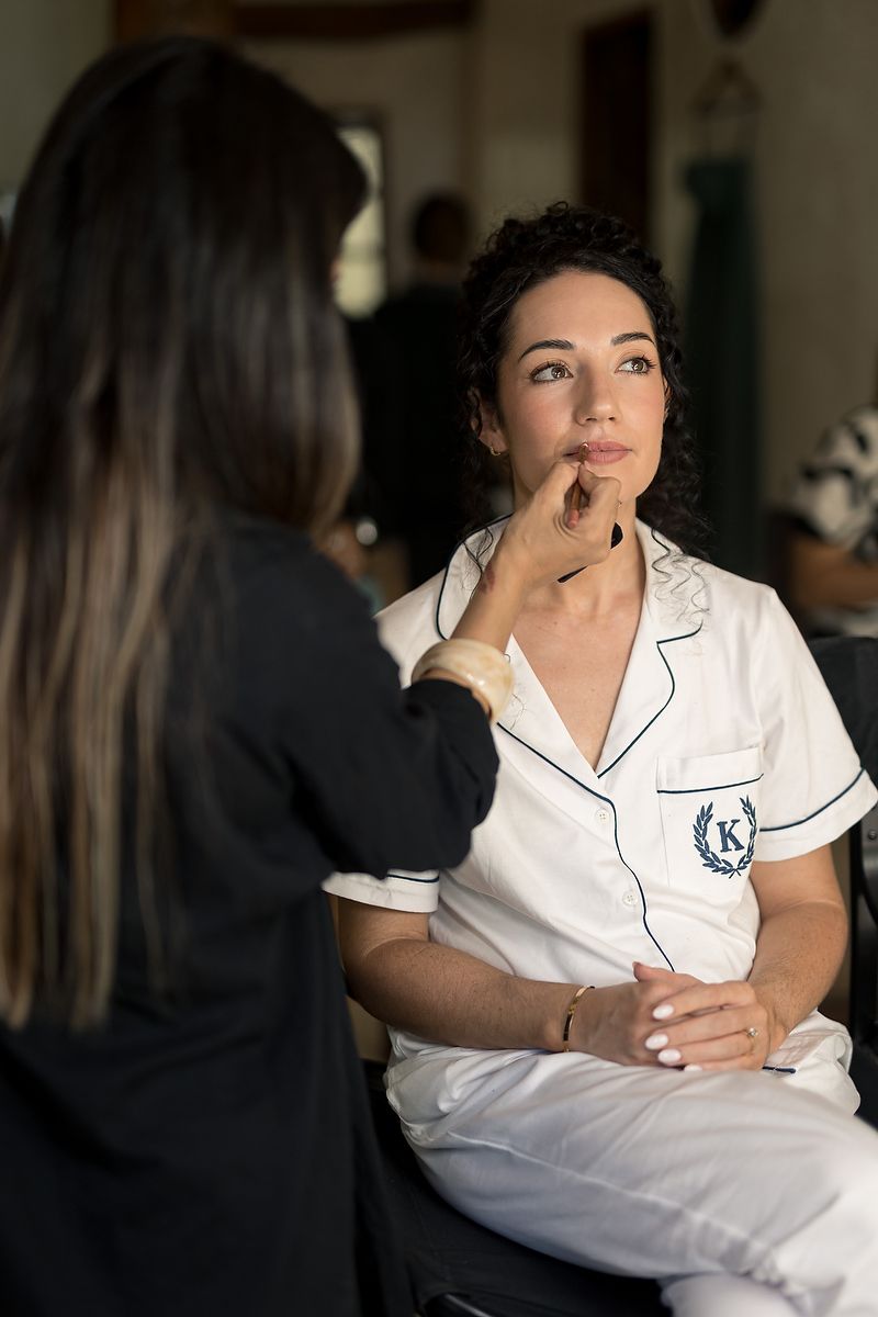 A makeup artist applies cosmetics to a person wearing white pajamas during a professional beauty session.