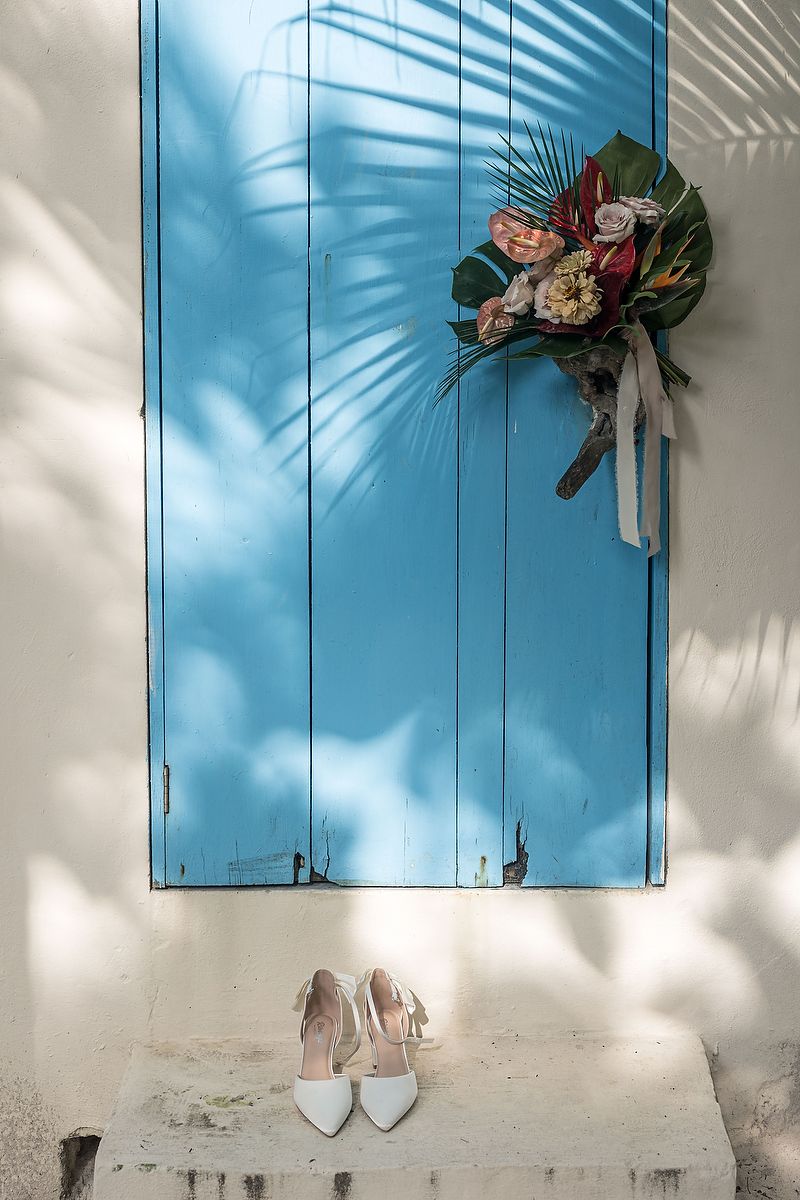 Bright blue shutters on a white wall with tropical flowers and palm shadows creating a beachy atmosphere.