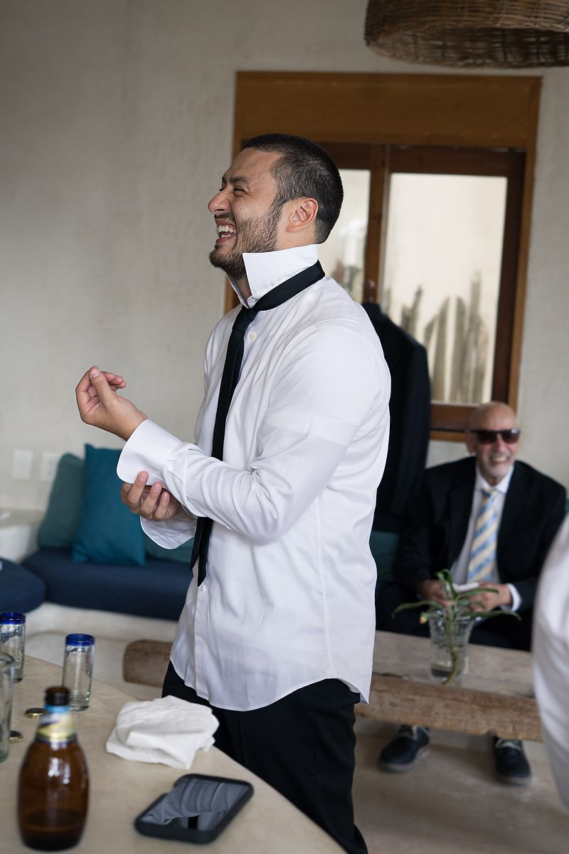 Groom getting ready at Mahayana Tulum, adjusting his shirt in a natural-lit villa during an intimate destination wedding in Tulum, Mexico.