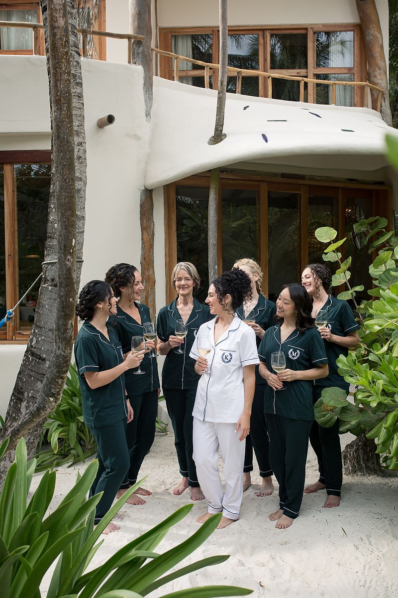 People in dark uniforms and white clothing gathered outside a building with palm trees and tropical landscaping.