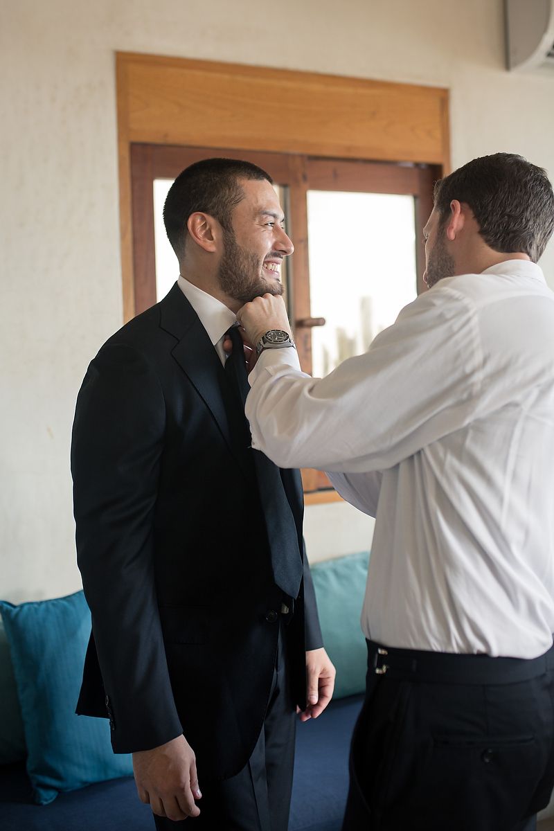 A sequence of four images showing two men in formal attire adjusting each other's ties and clothing.