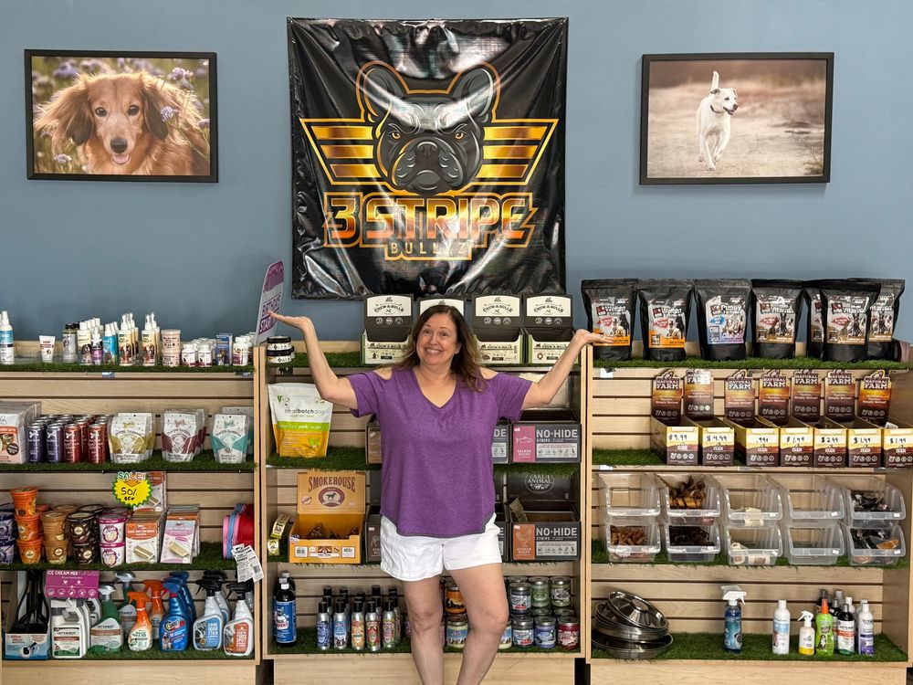 Retail shelves stocked with pet food, treats and supplies against a light blue wall with framed dog photos.