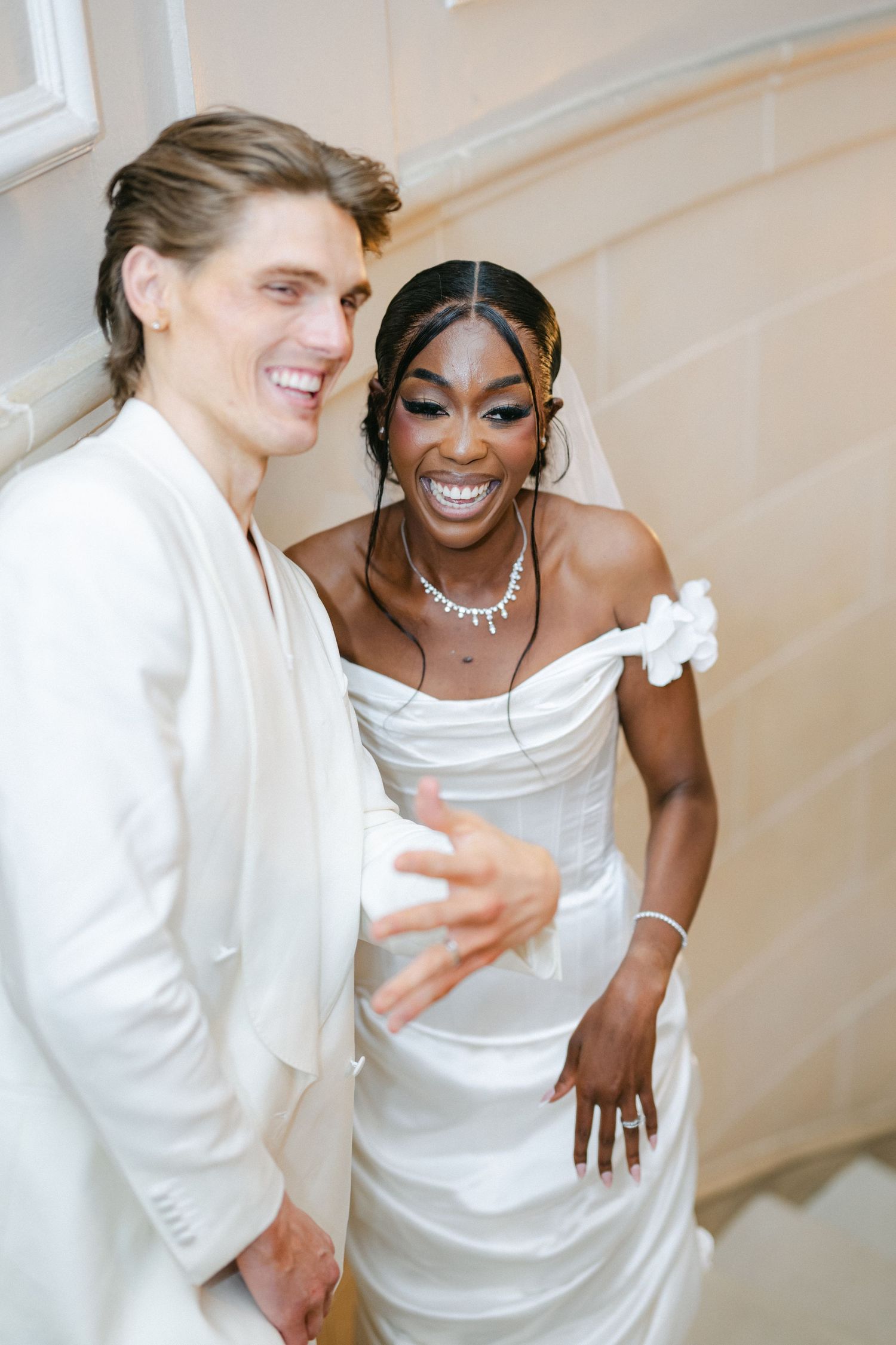 A joyful couple in white wedding attire share a candid laughing moment together during their celebration.