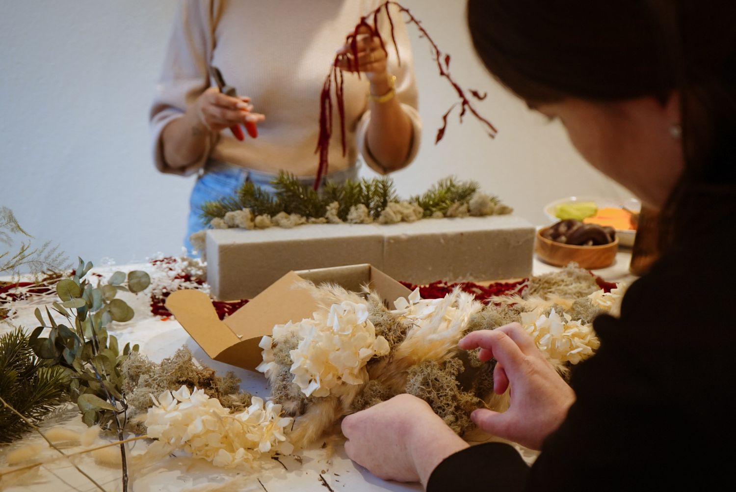 People working on floral arrangements with moss and branches at a crafting table.