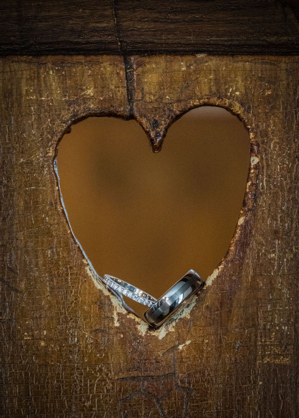 A series of heart-shaped cutouts in rustic wooden panels with rings displayed inside.