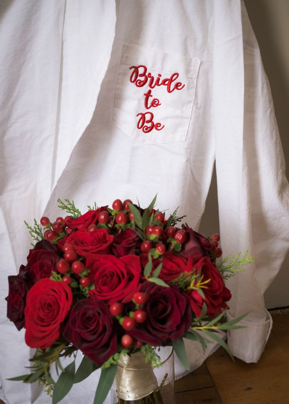 Red roses and berries arranged with white linens featuring embroidered text.