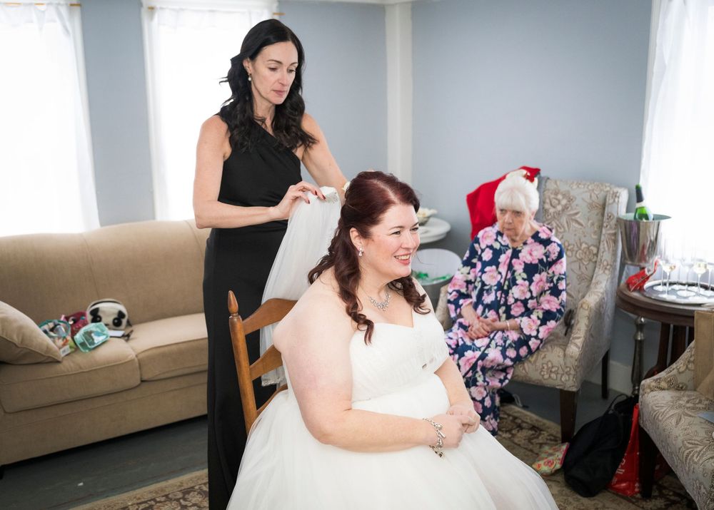 A bride in a white wedding gown poses during preparation photos in a bright room.
