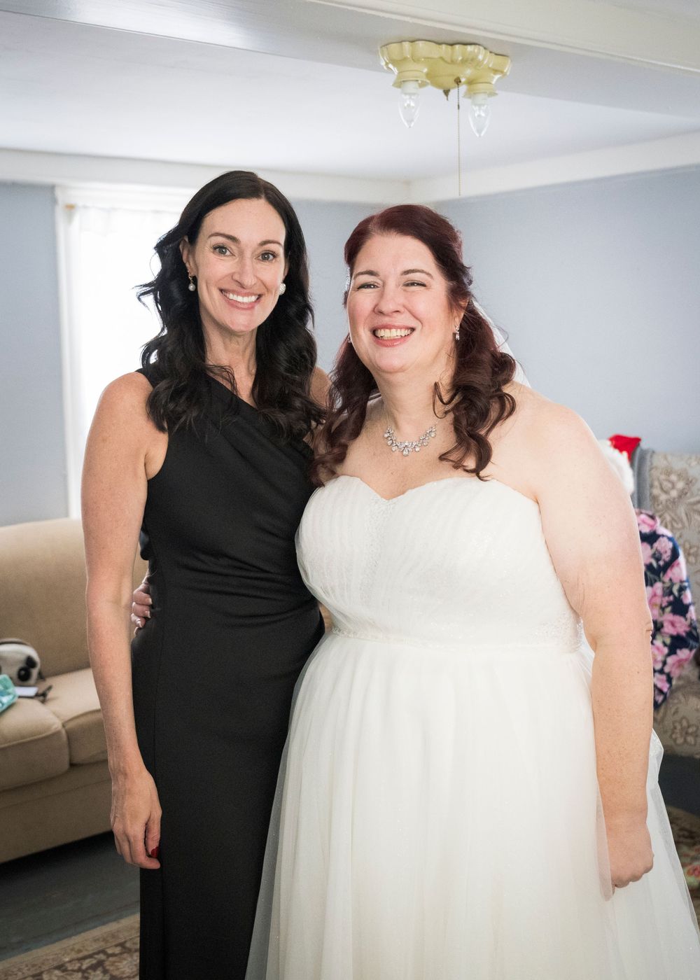 Two people pose together in a bright room with white walls and modern decor.