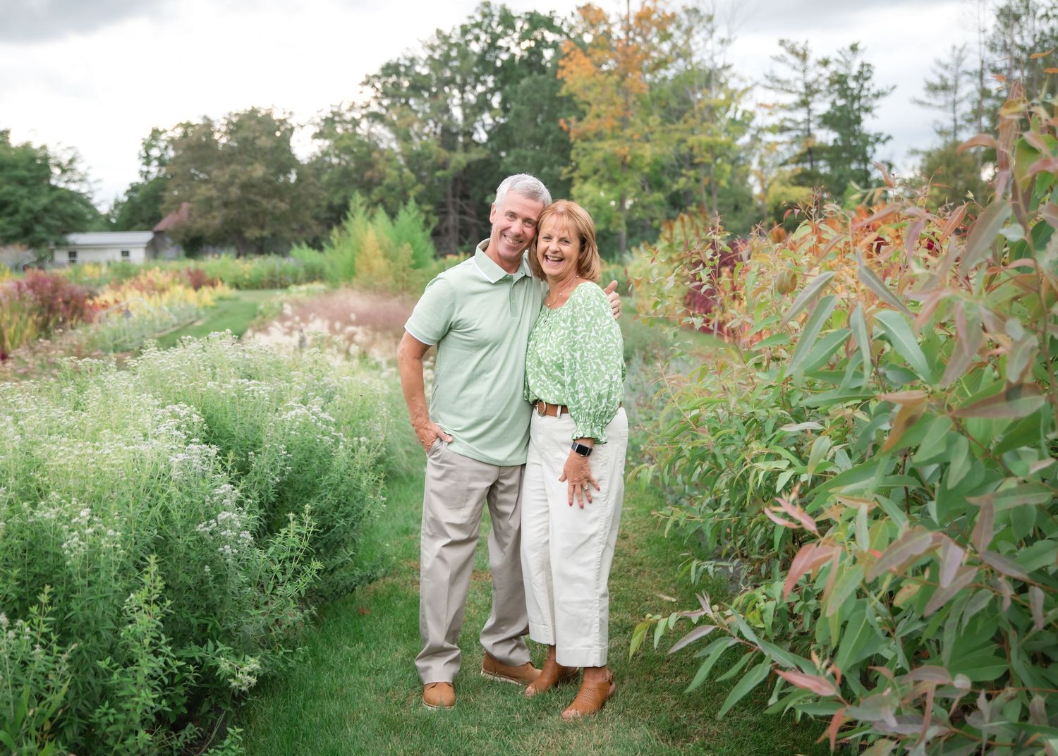 A couple poses together in a lush garden setting surrounded by flowering plants and greenery during golden hour.