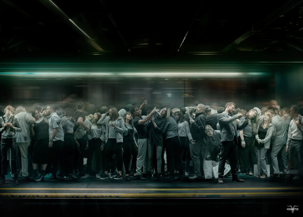 A crowd of people stand together on a dark stage illuminated by eerie green lighting in a theatrical performance.