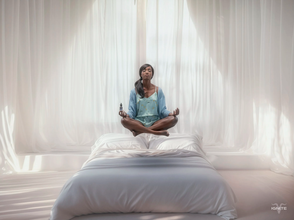 A person in blue clothing sits cross-legged on a white bed in a bright, minimalist room.