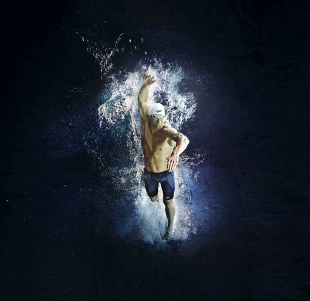 Athletic figure emerges from an explosive splash of water against a dark background in a dynamic sports pose.