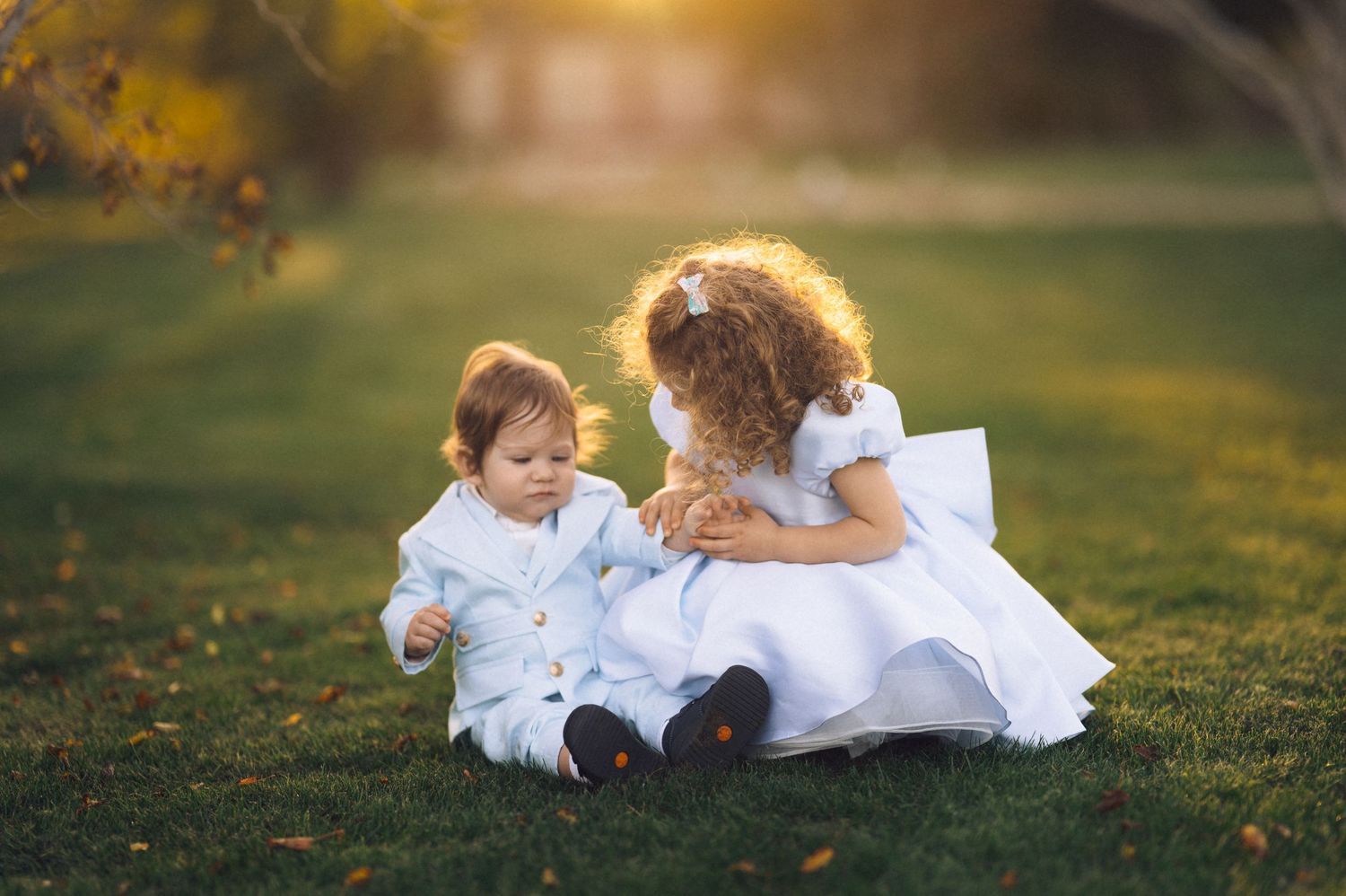 A small child in a white outfit plays and dances on grass during golden hour lighting.