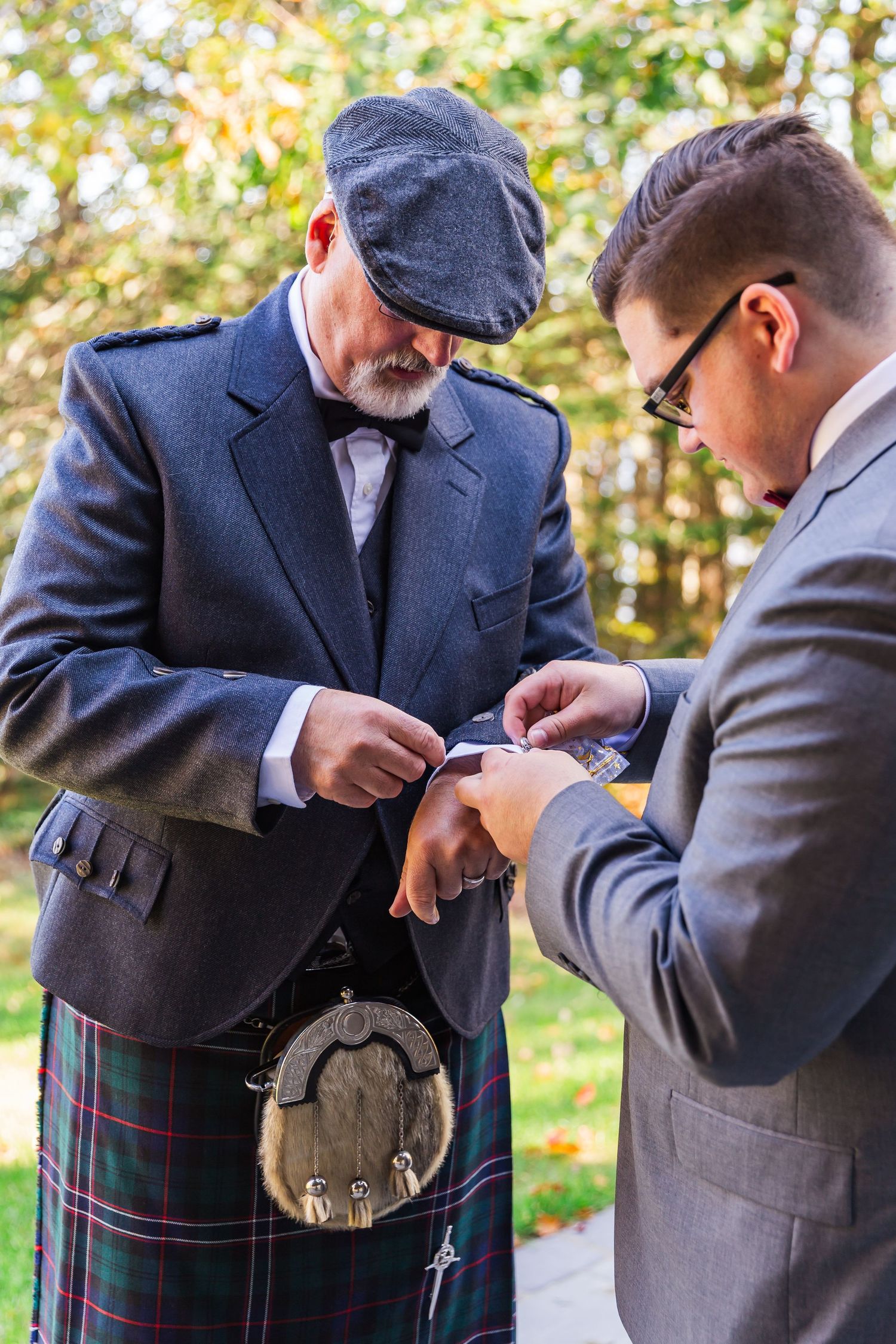 Men in formal attire and kilts adjust their traditional Scottish sporrans during a formal gathering outdoors.