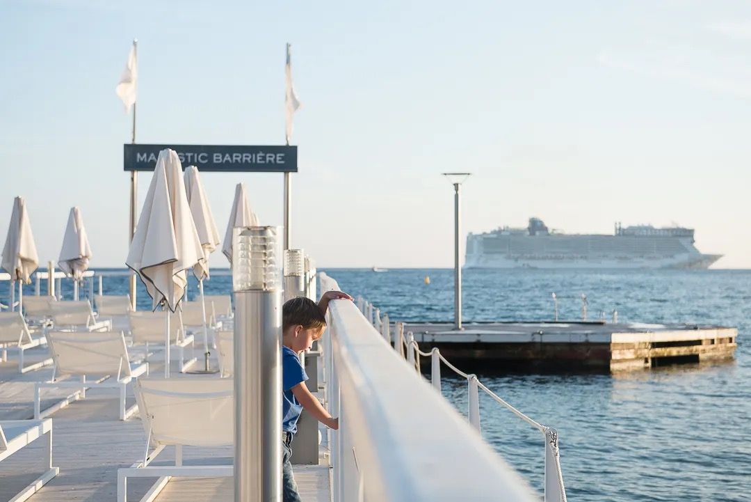 A child looking out over the marina towards a cruise ship on a sunny morning.