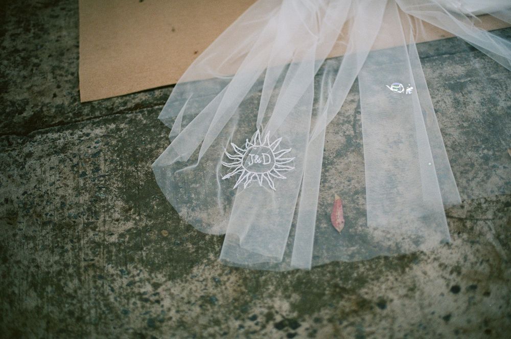 Delicate white wedding veil with embroidered floral details laying on a concrete surface.