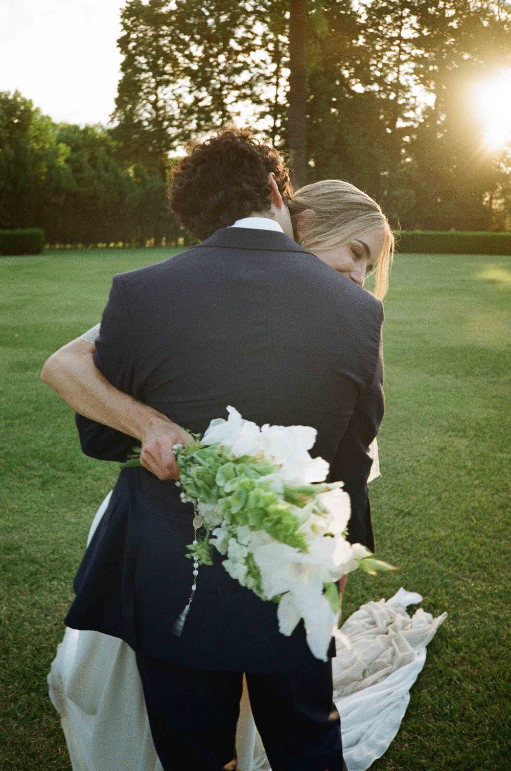 A couple embraces in a romantic outdoor setting during golden hour with white flowers between them.