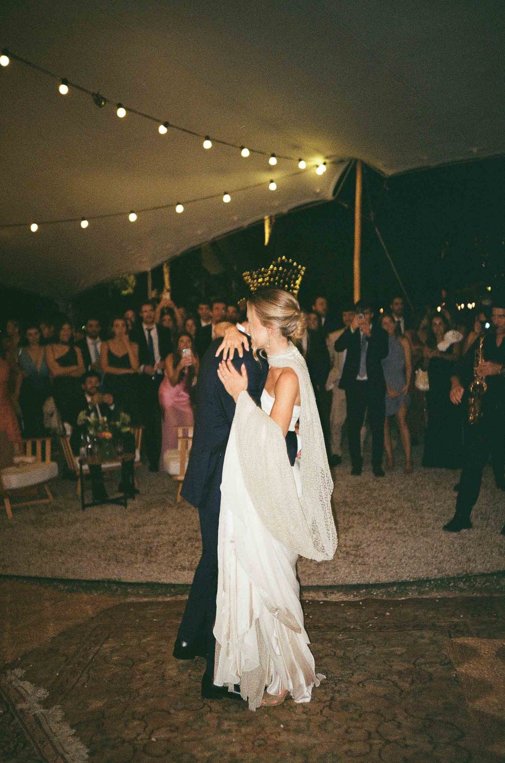 A couple dances under string lights at an outdoor evening wedding reception.