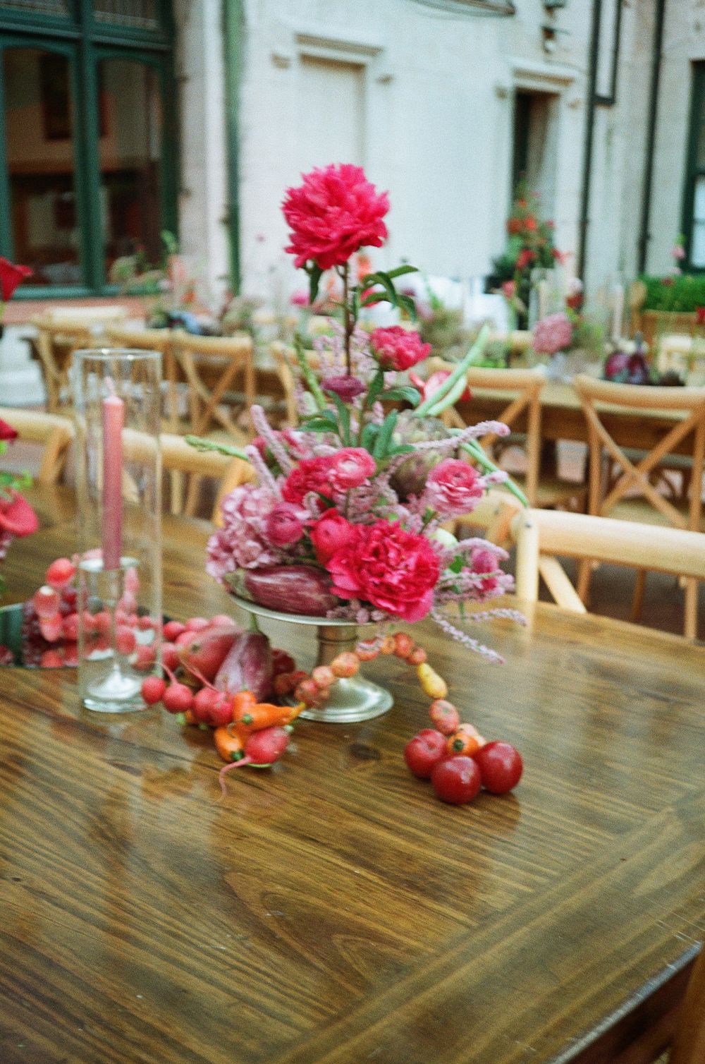 Pink carnations and red apples create an elegant table centerpiece on a rustic wooden surface at an outdoor restaurant.
