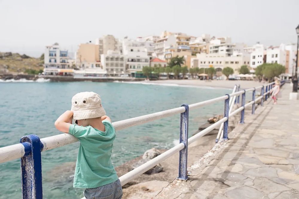 A person walks along a seaside promenade with white railings and blue ocean views in the background.