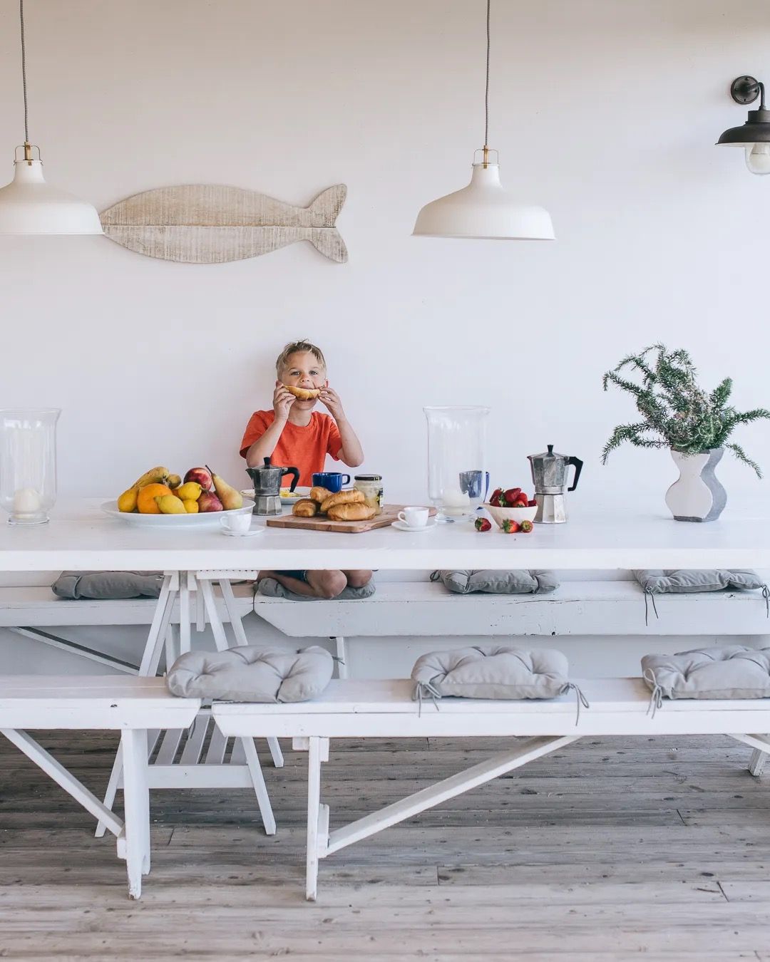 A woman prepares food in a bright, coastal-style white kitchen with modern décor and natural lighting.