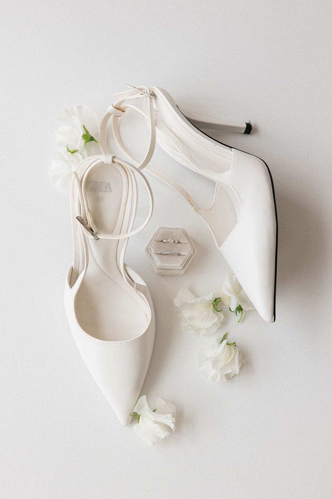 White bridal heels with delicate floral accents arranged in a minimalist composition against a light background.