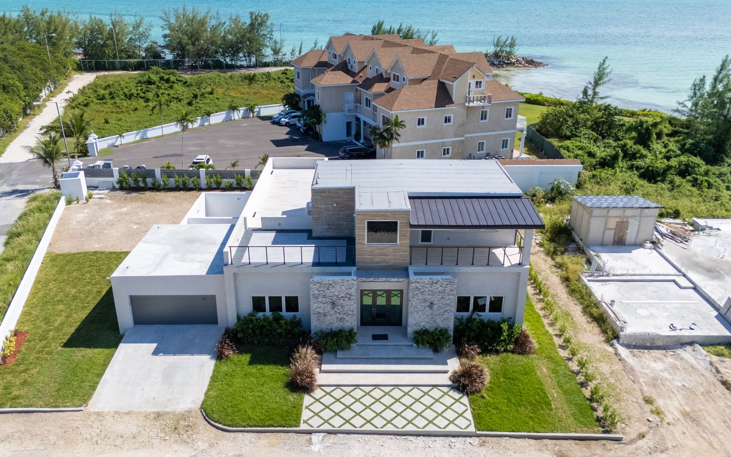 Aerial view of modern coastal homes with solar panels and white roofs along a sunny beachfront property.