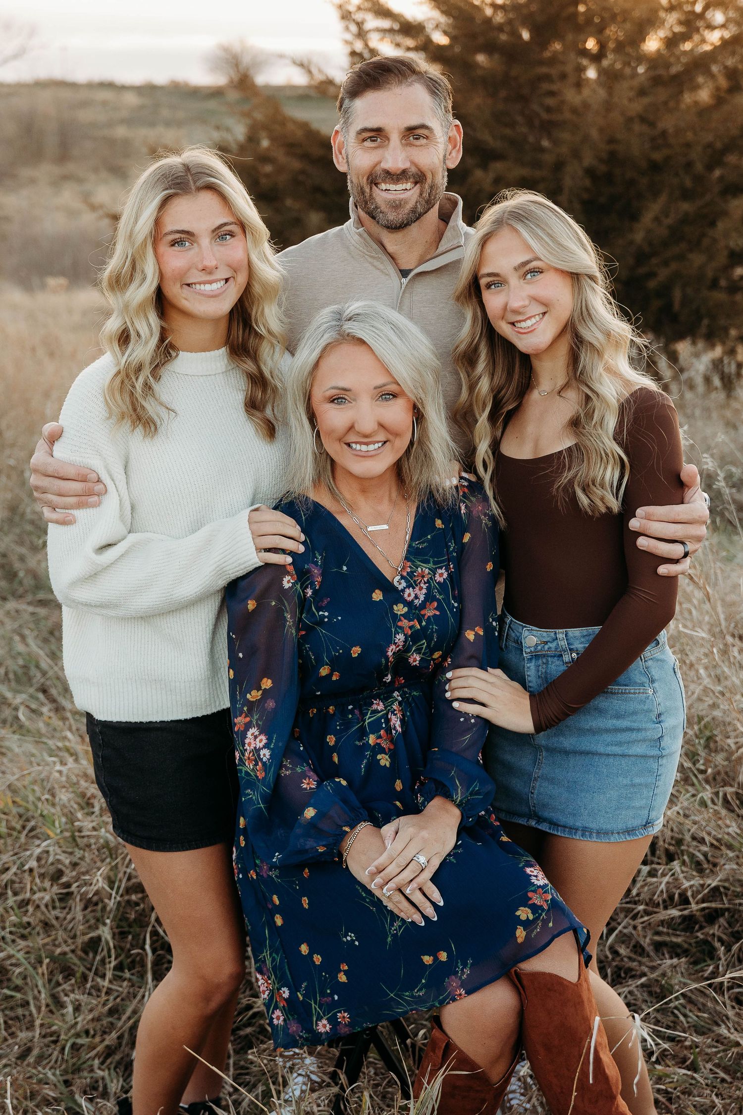 A family poses together outdoors in casual attire during golden hour in a field of tall grass.