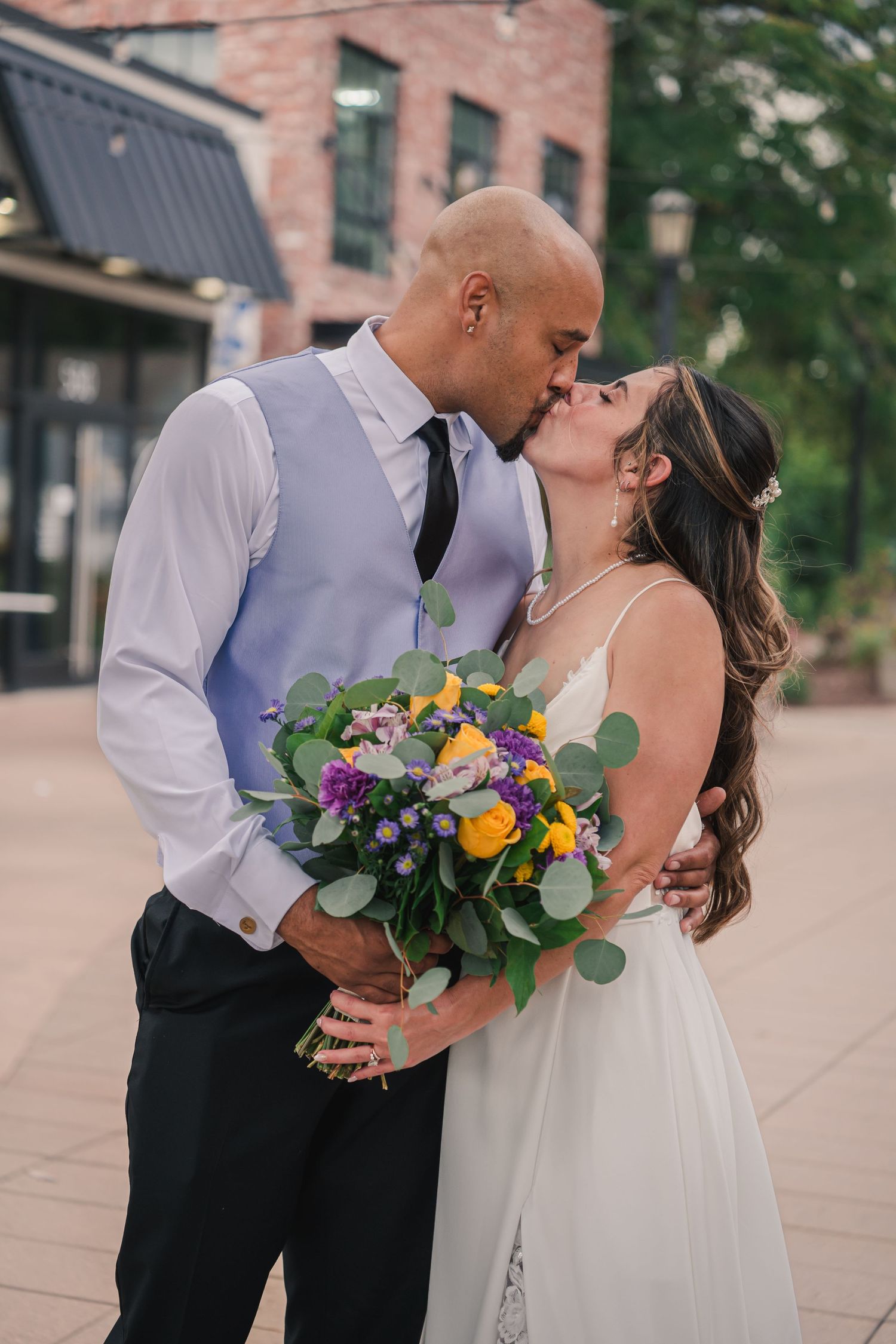 A couple in wedding attire share romantic kisses in a series of three photos on a brick-paved walkway with flowers.