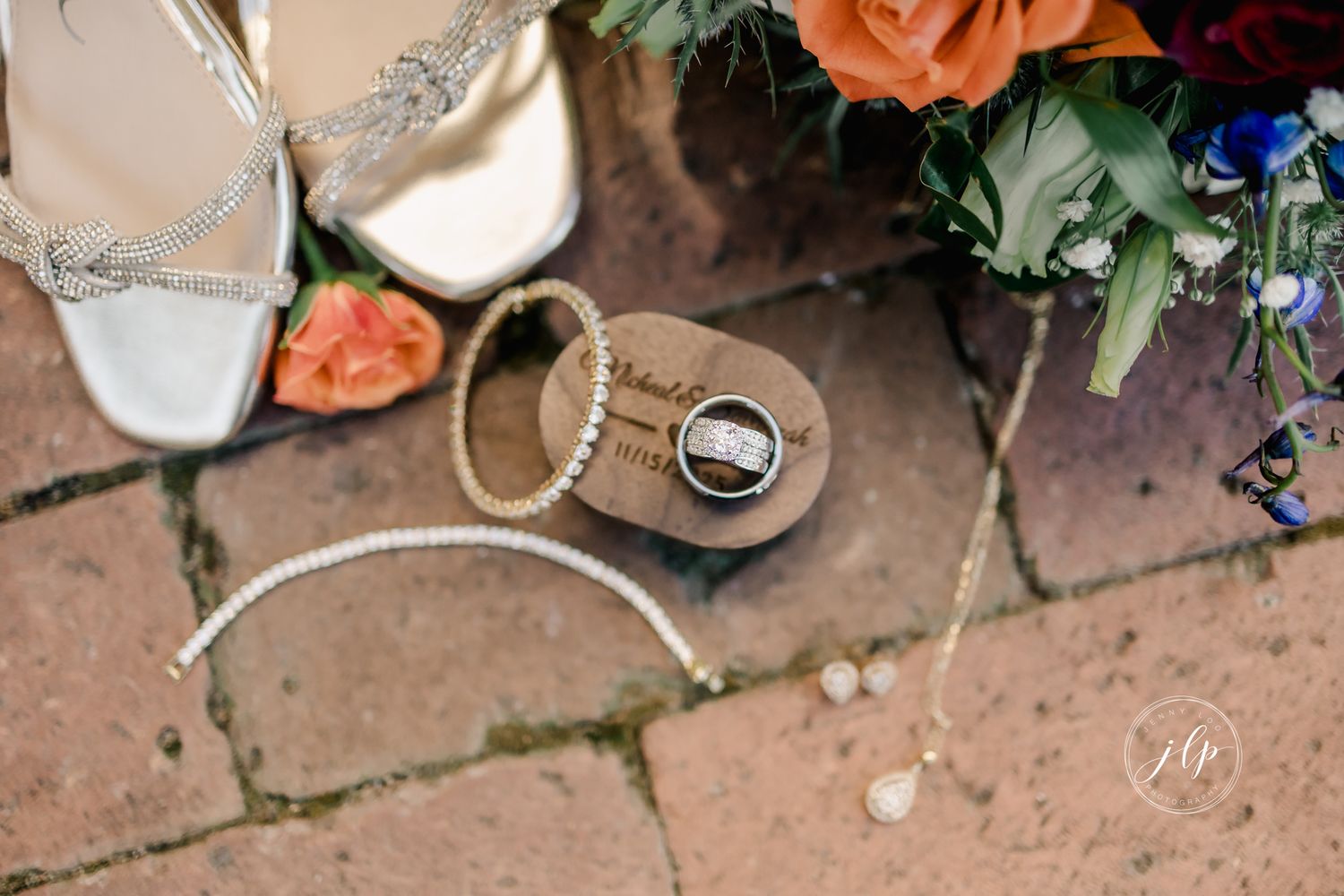 Wedding details including white bridal shoes, rings, and colorful flowers arranged on terracotta tiles.