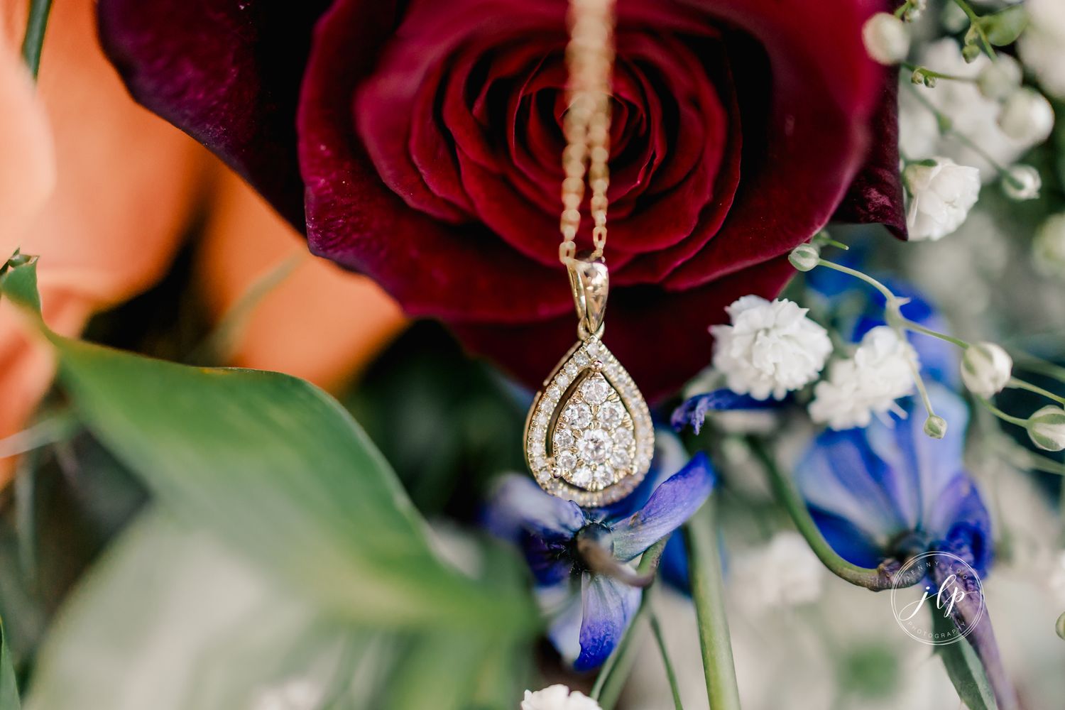 Close-up of deep red roses with blue flowers and delicate jewelry details.