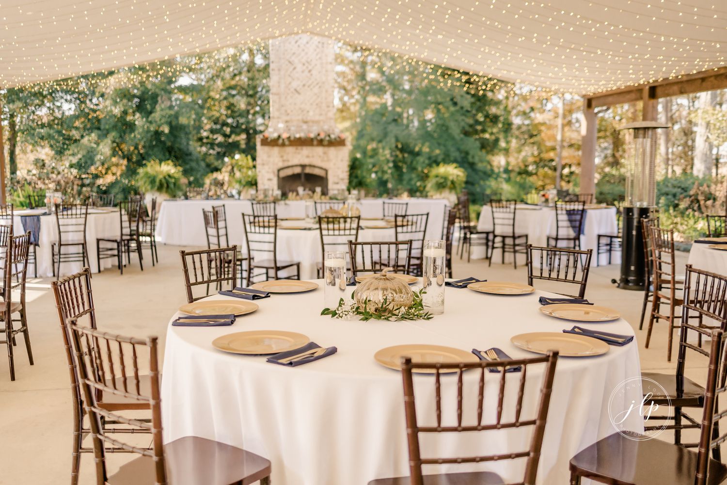 An elegant wedding reception setup with round tables, white linens, and Chiavari chairs in an outdoor covered venue.