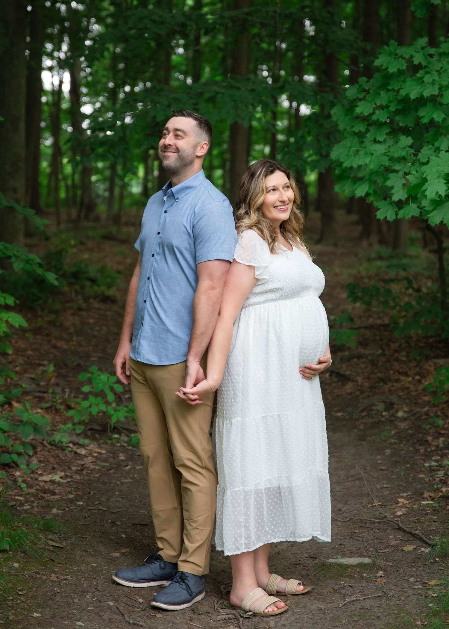 A couple shares a romantic moment on a wooded trail surrounded by lush green foliage on a summer day.