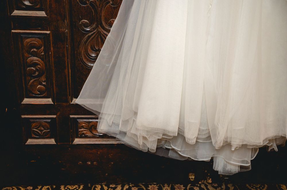 Close-up view of a white tulle wedding dress hem against an ornate wooden background.