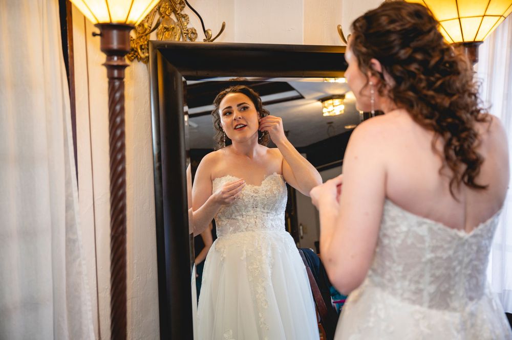 A bride in a white strapless gown admires her reflection in a mirror while getting ready.