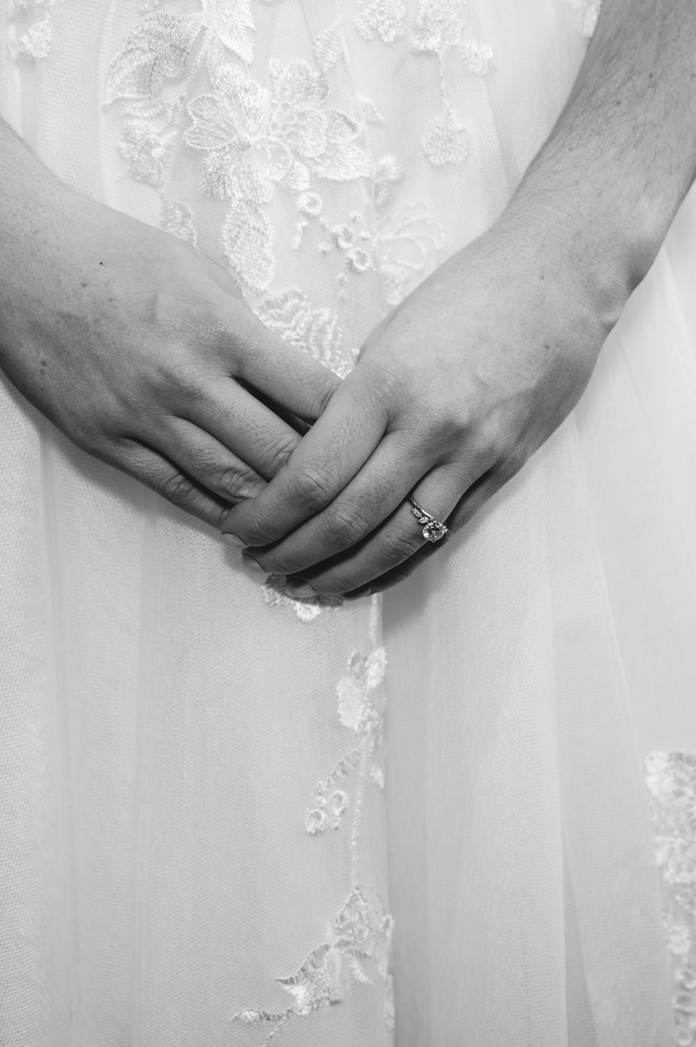 A series of black and white photos showing hands with engagement rings against white lace wedding dress fabric.
