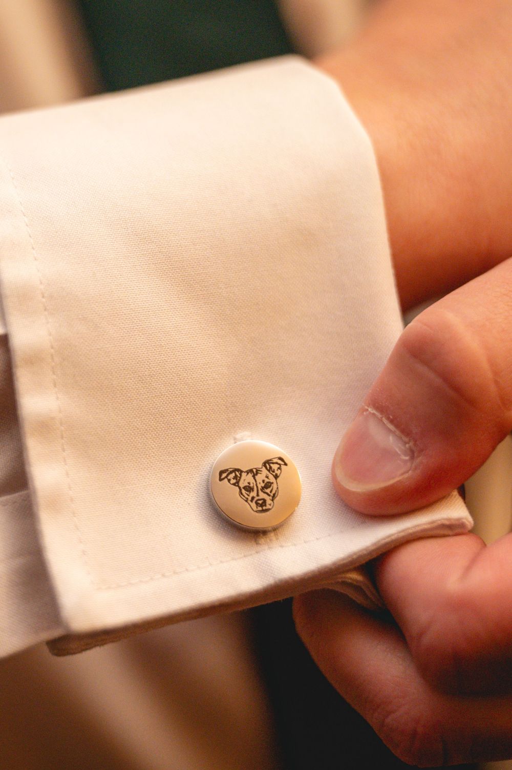 Detailed shot of ornate cufflinks being fastened into white shirt cuffs.