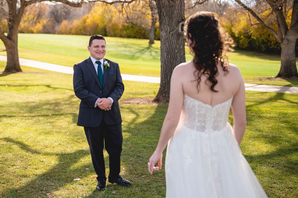 Wedding party poses outdoors in autumn sunlight with golden trees and grass in the background.