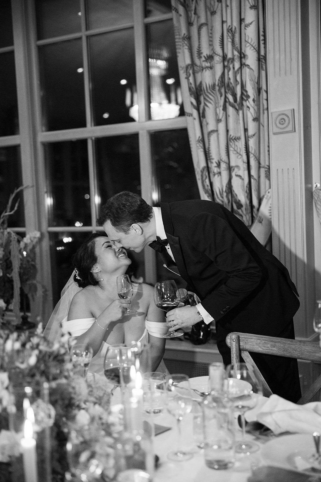 A romantic black and white wedding reception scene with a couple sharing an intimate moment at an elegant candlelit table.