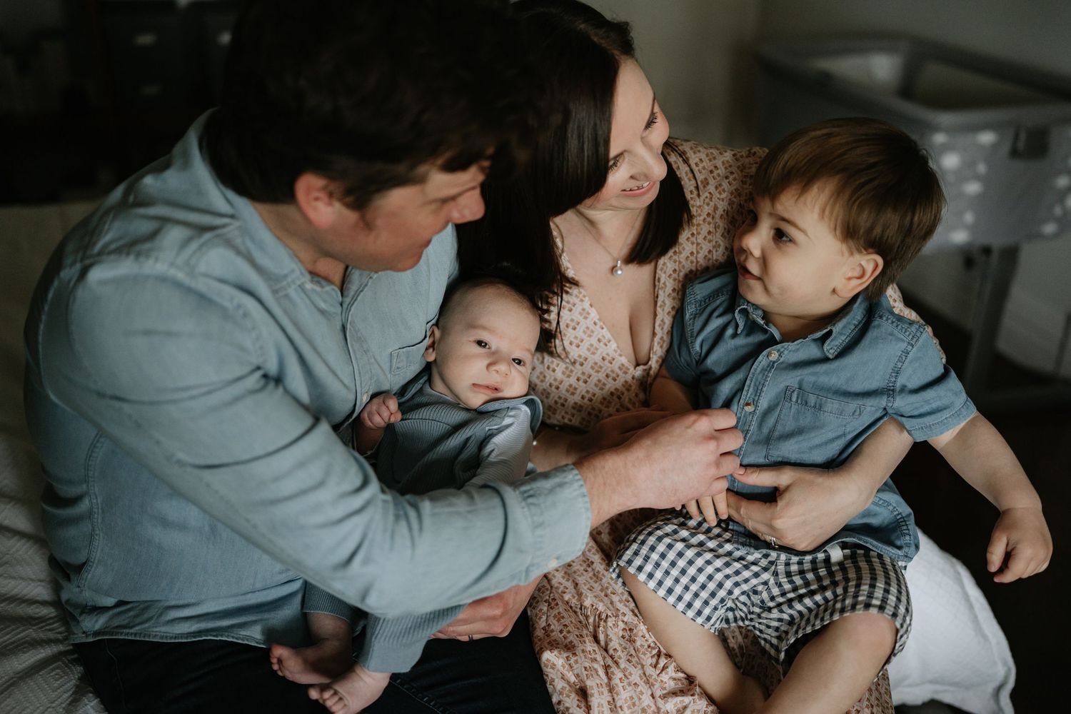 Mother, father, toddler and baby on a bed in beautiful mid-morning light during an indoor newborn photography session in Perth