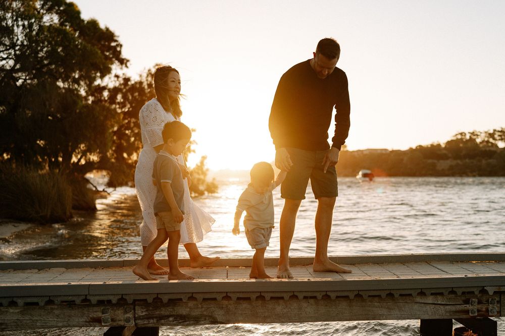 A family walking along a bridge with the sun setting in the background during a Perth outdoor family photography photoshoot.