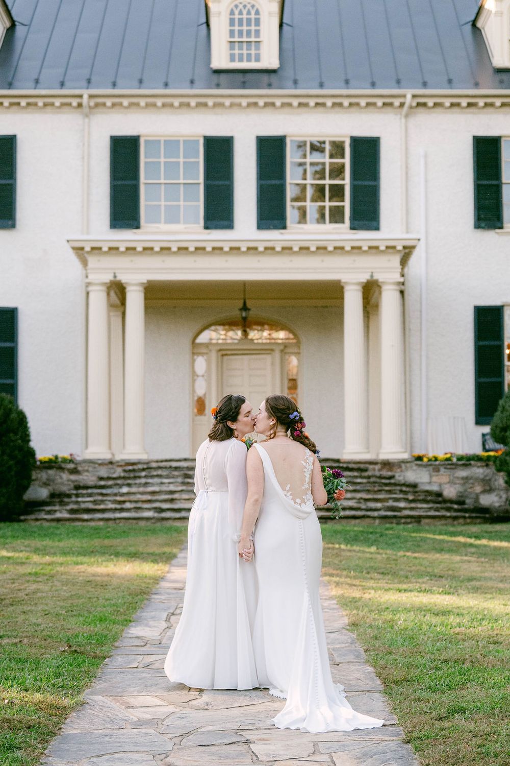 Elegant white wedding dresses photographed in front of a historic white colonial building with columns.