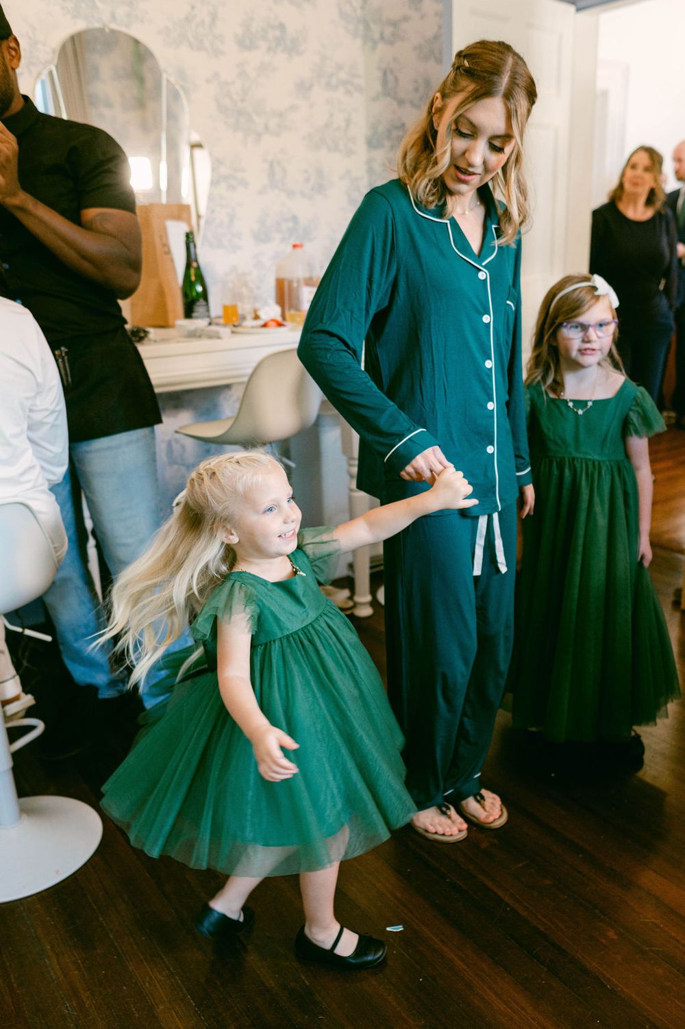 Group wearing dark robes and green dresses dancing and celebrating on hardwood floors.