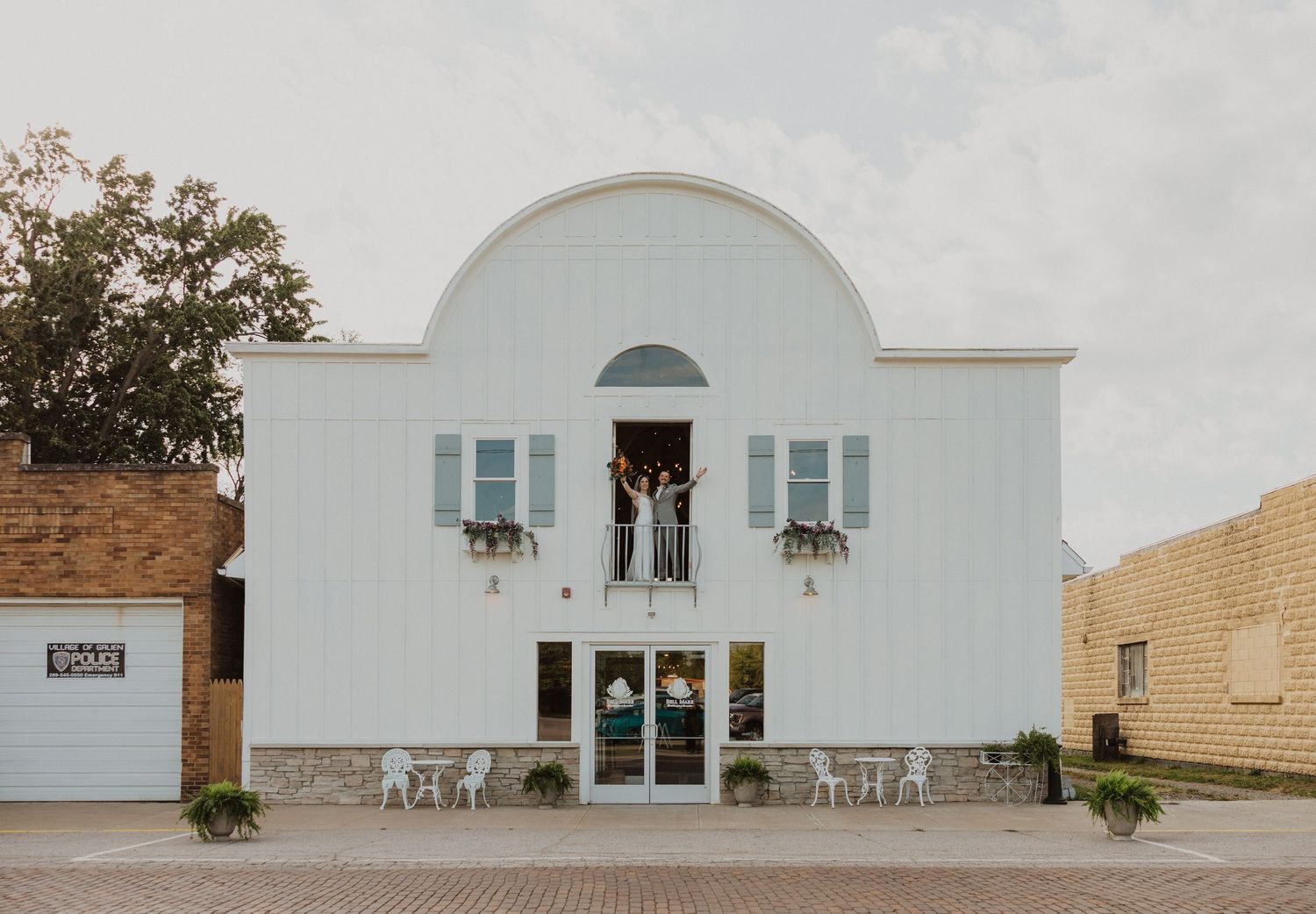 Bride and groom cheering on the upper balcony of  Bell Mare in Galien, Michigan, with blue shutters and flower boxes.